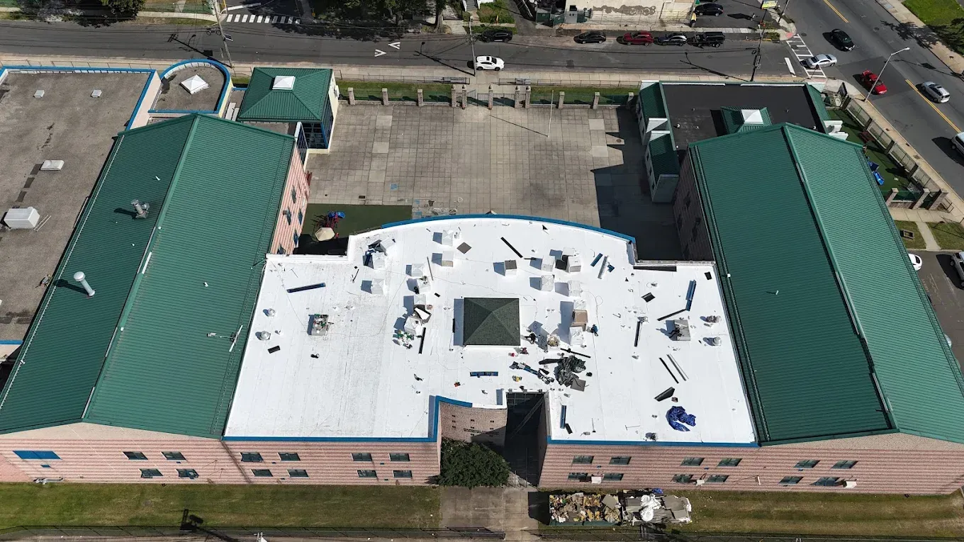 Aerial view of a building with green roof and light pink walls; a large open space.