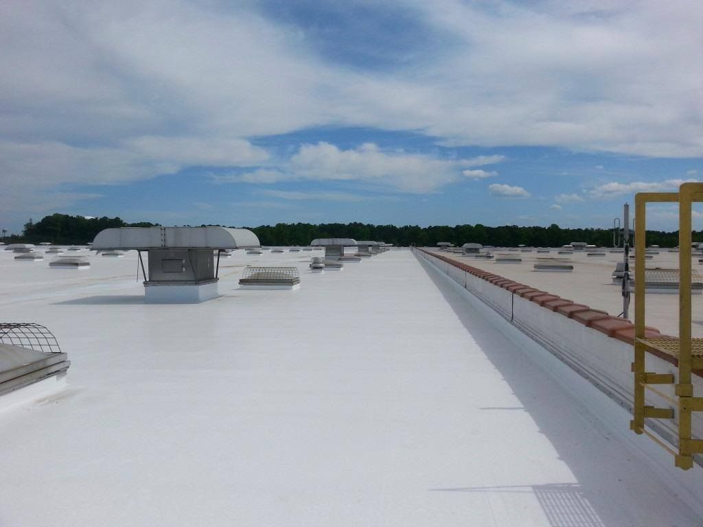 White commercial roof with vents, safety rails, and blue sky.