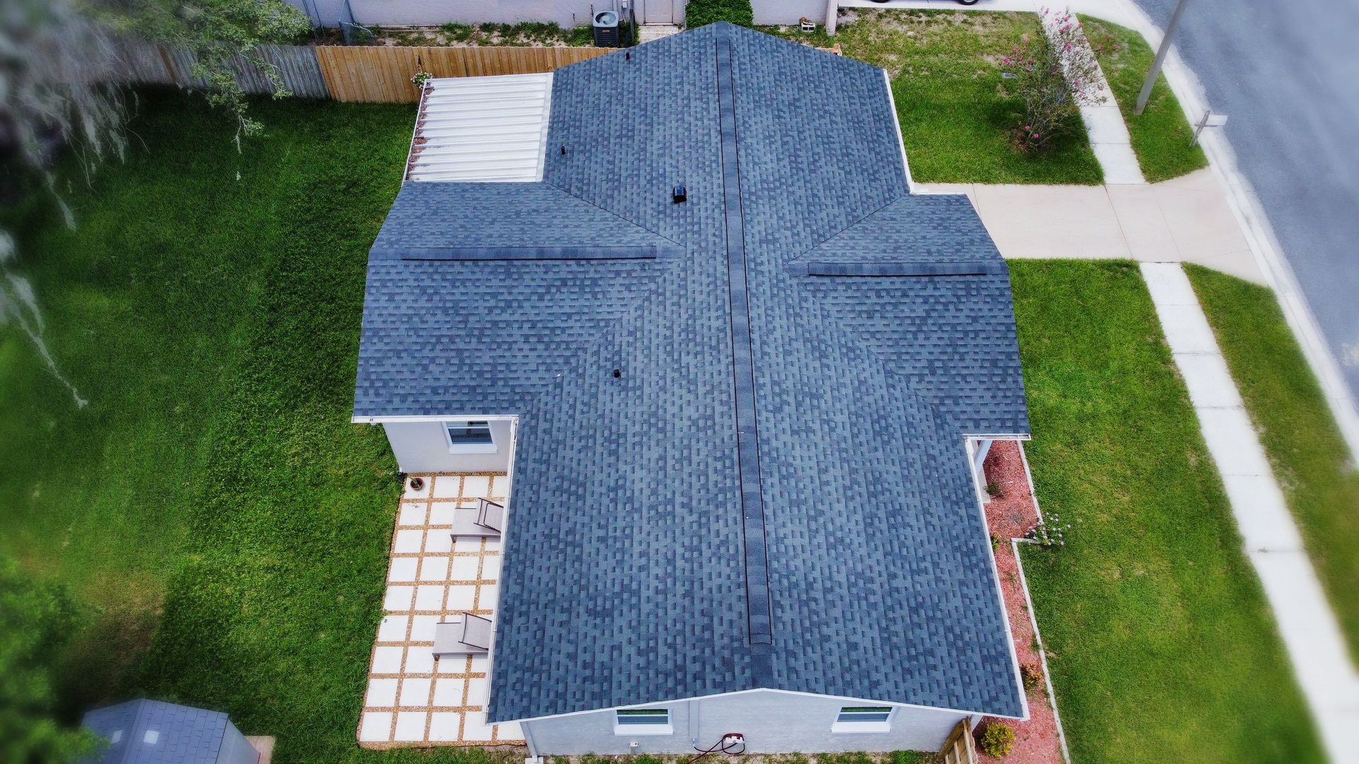 Overhead view of a house with a gray roof, surrounded by green grass and a sidewalk.