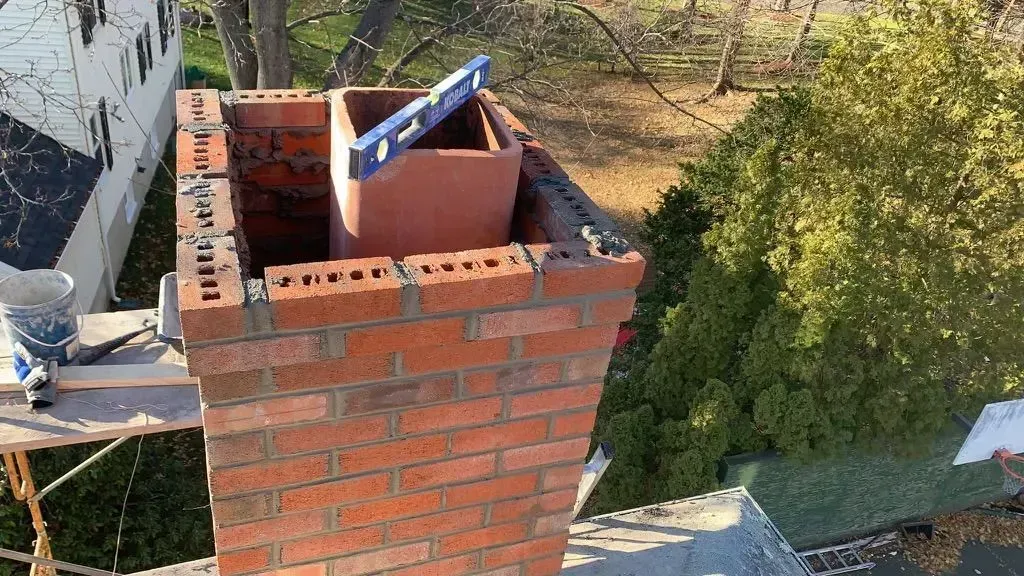 Brick chimney being built; worker uses a level.