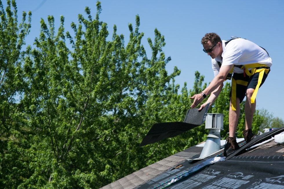 Roofer in safety harness on a roof replacing shingles on a sunny day.