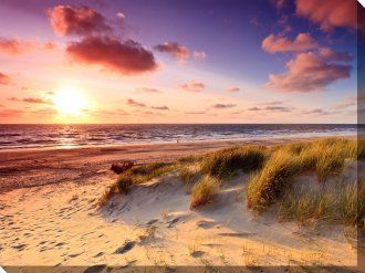 A sunset over a sandy beach with dunes in the foreground.