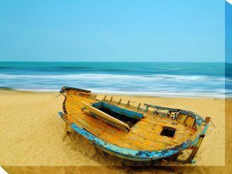 An old wooden boat is sitting on a sandy beach near the ocean.