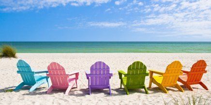 A row of colorful lawn chairs are lined up on a beach.