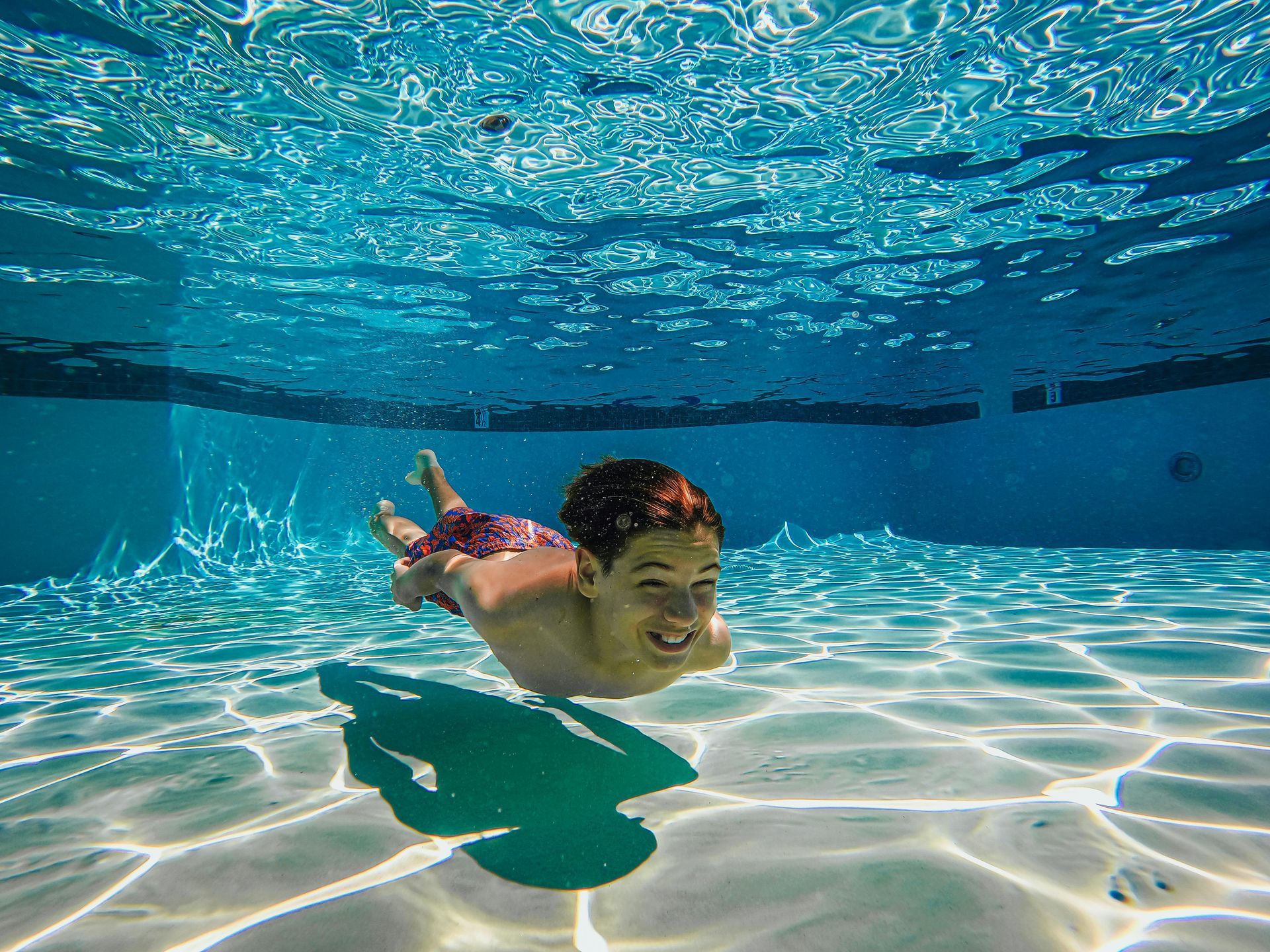A young boy is swimming underwater in a swimming pool.
