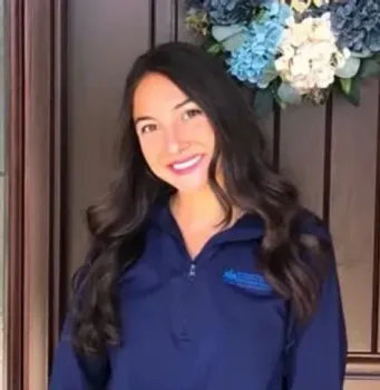 A woman in a blue jacket is standing in front of a door with a wreath on it.