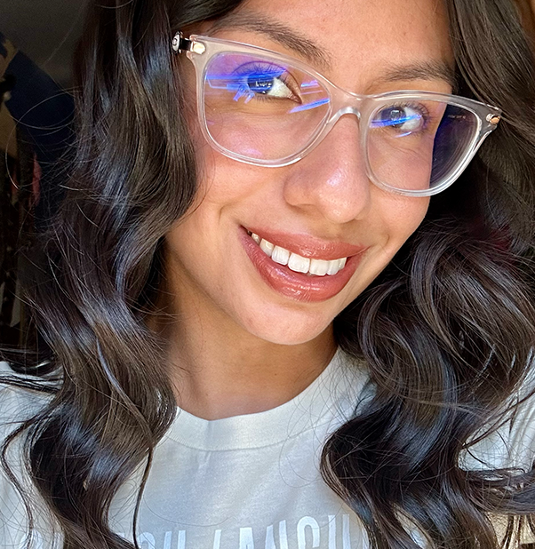 A woman is standing on a cliff overlooking the ocean at sunset.