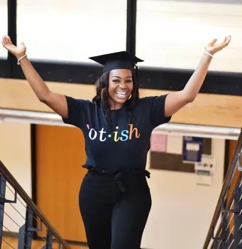 A woman in a graduation cap and gown is wearing a shirt that says ot-ish