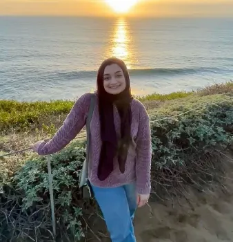 A woman is standing on a cliff overlooking the ocean at sunset.