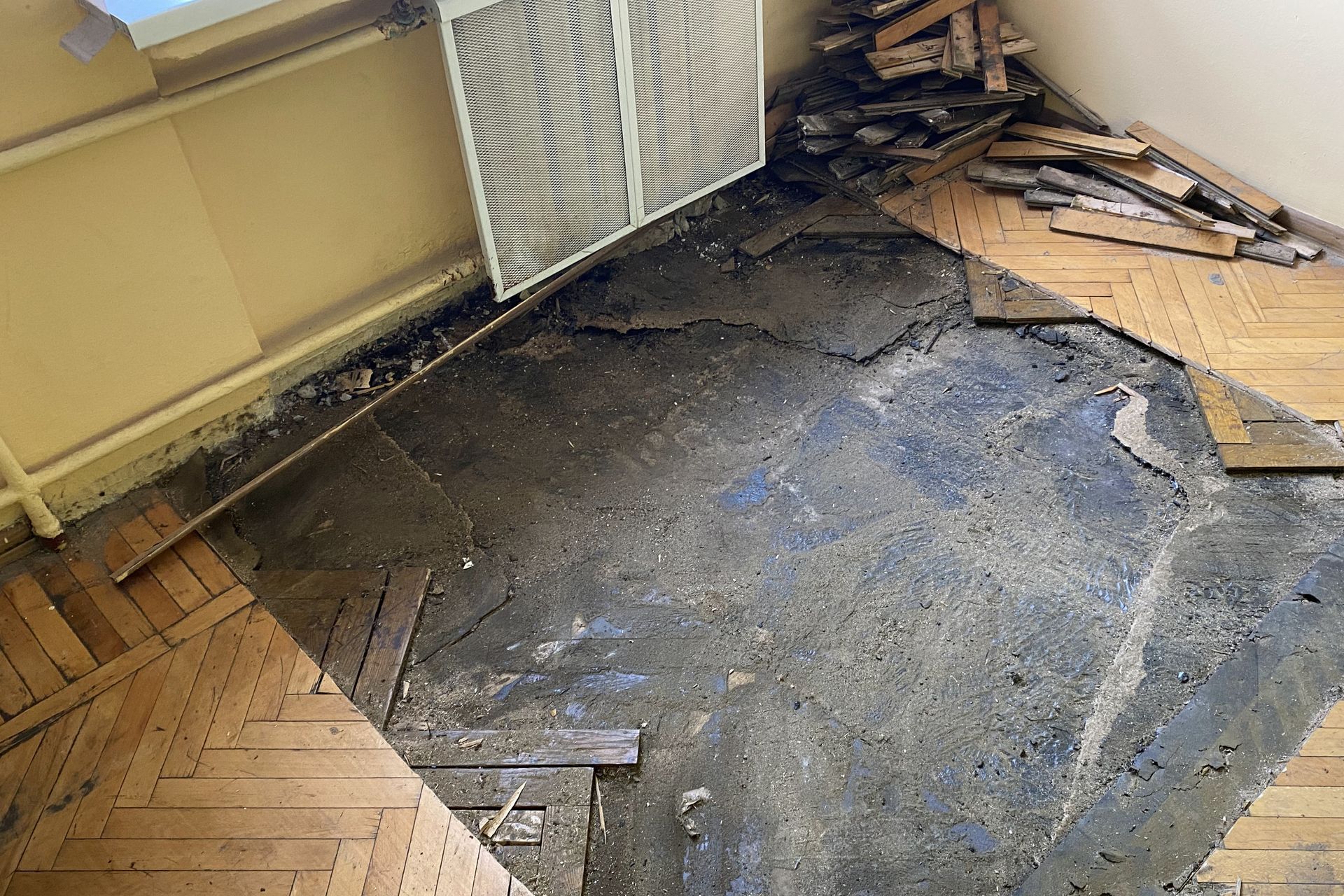 Damaged room floor with torn carpet, exposed underlayment, and scattered debris near a radiator
