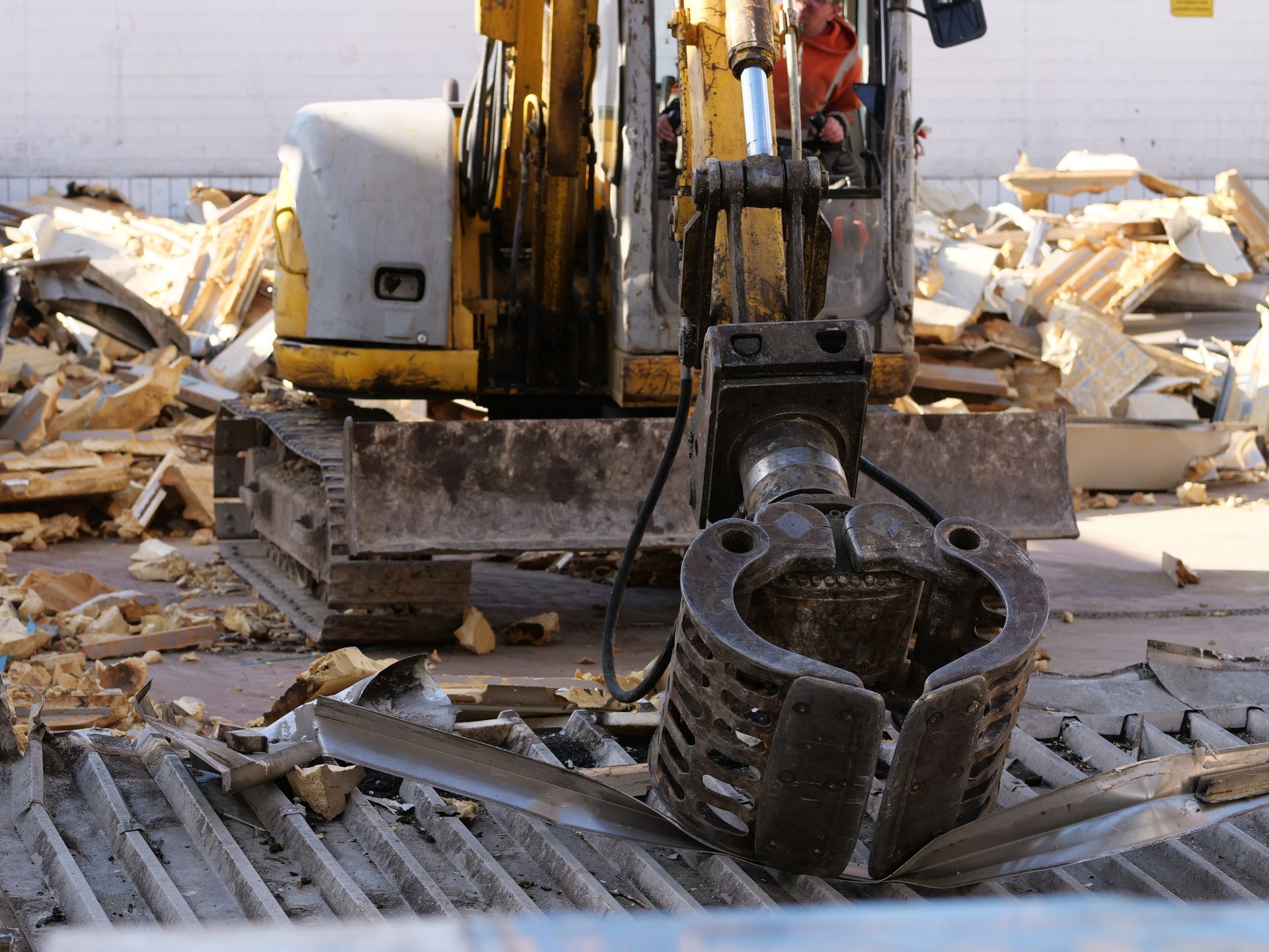 Excavator with claw working over a pile of broken wood and debris at a construction site
