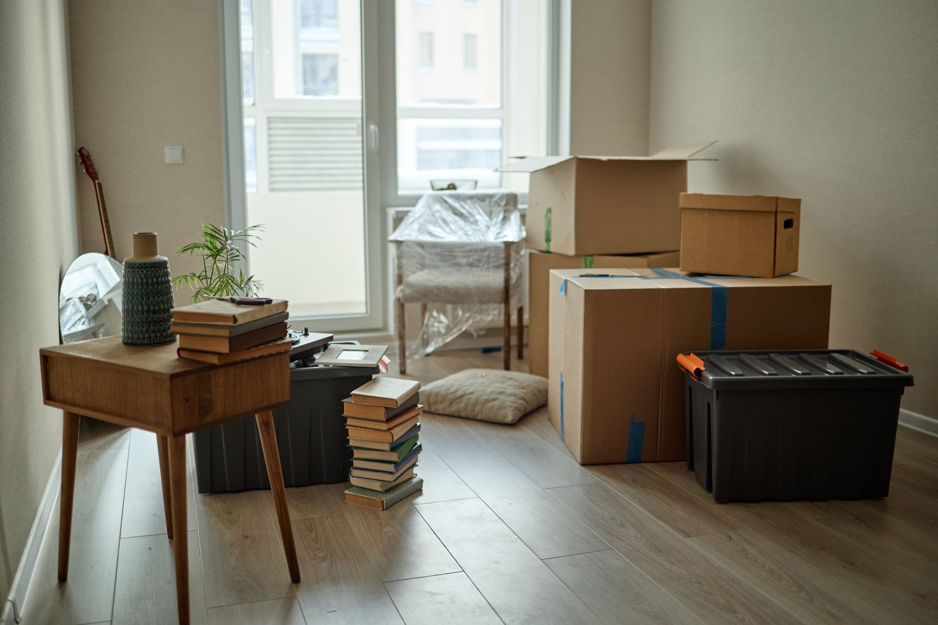Moving boxes and household items in a bright room near a window, suggesting packing or moving.