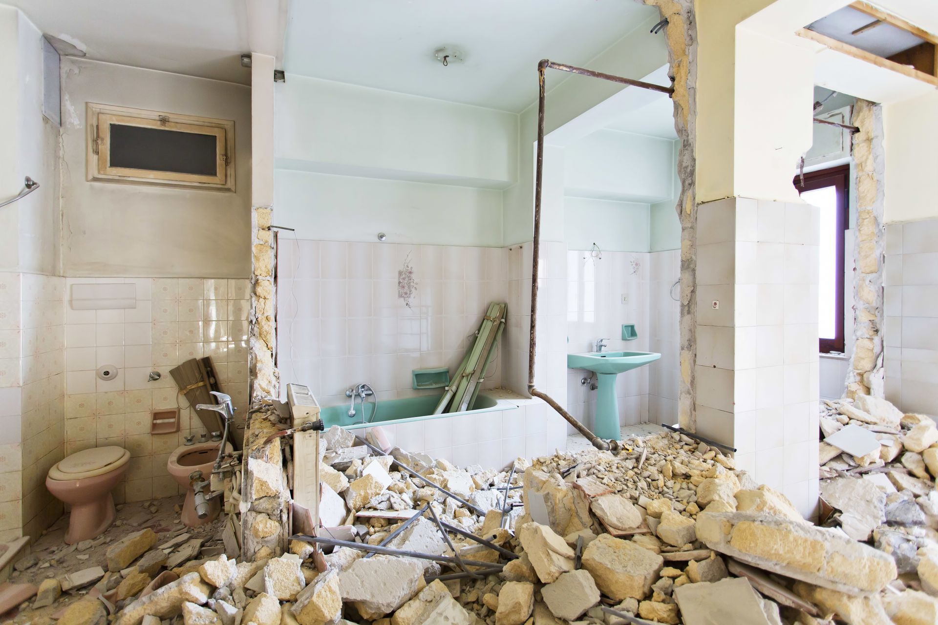 Bathroom damaged by demolition debris, with broken walls, rubble on the floor, and a bathtub visible.