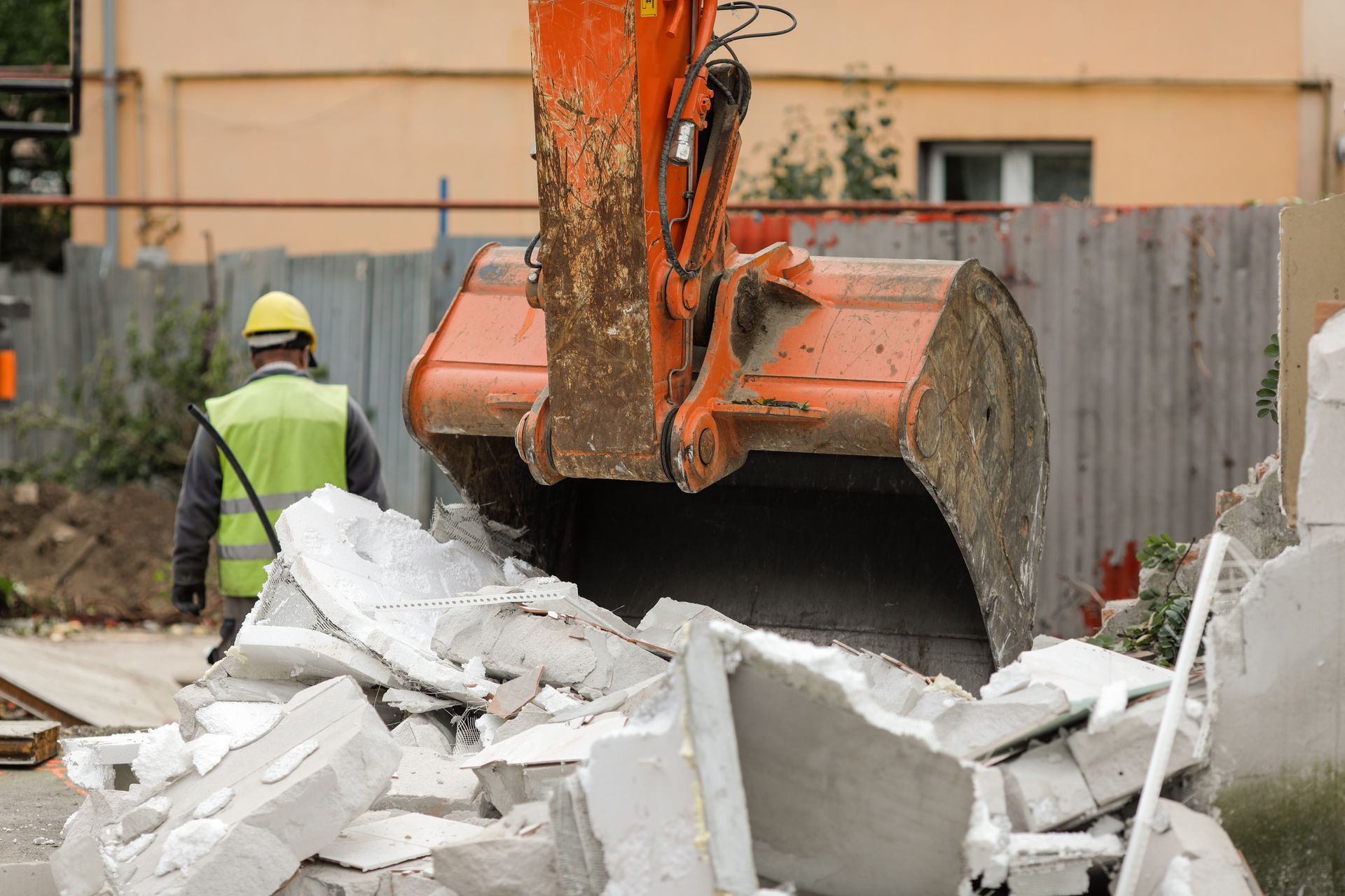 Construction worker near excavator clearing white rubble at a demolition site