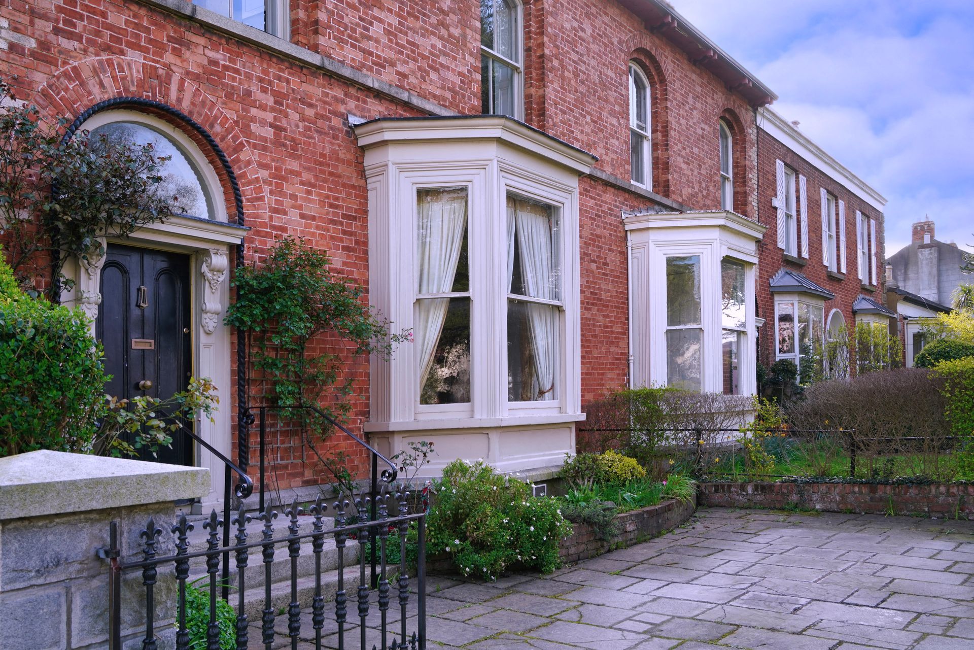 A row of brick houses with bay windows and a wrought iron fence.