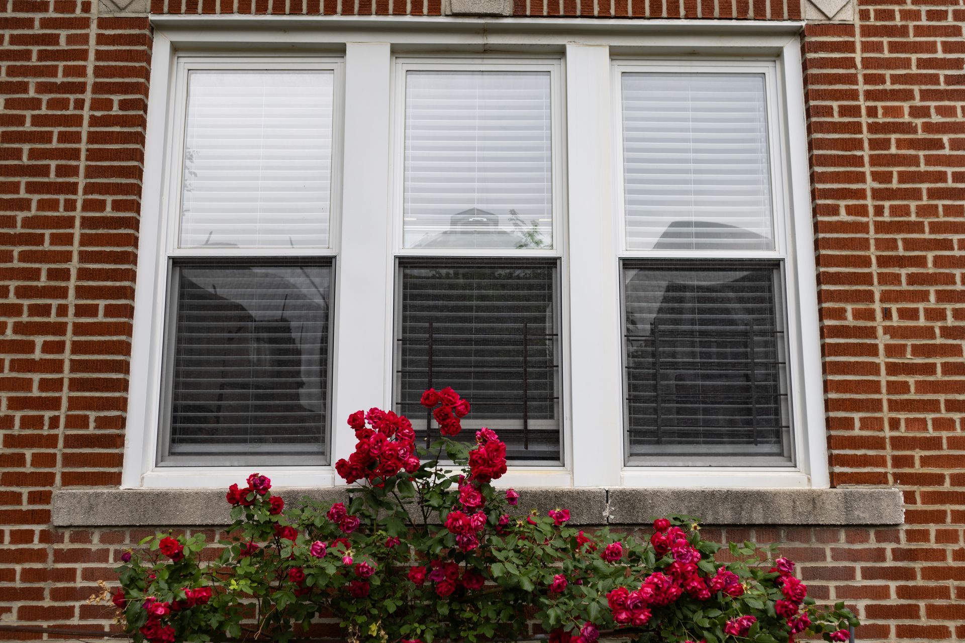 A brick building with a window with blinds and flowers in front of it.