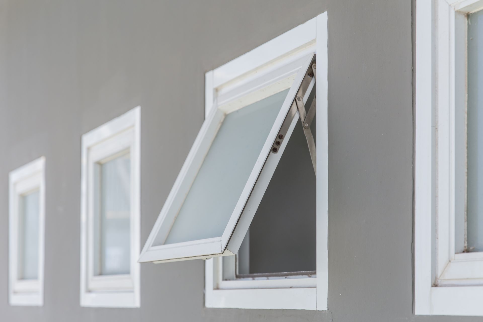 A row of white windows on a gray wall with one window open.