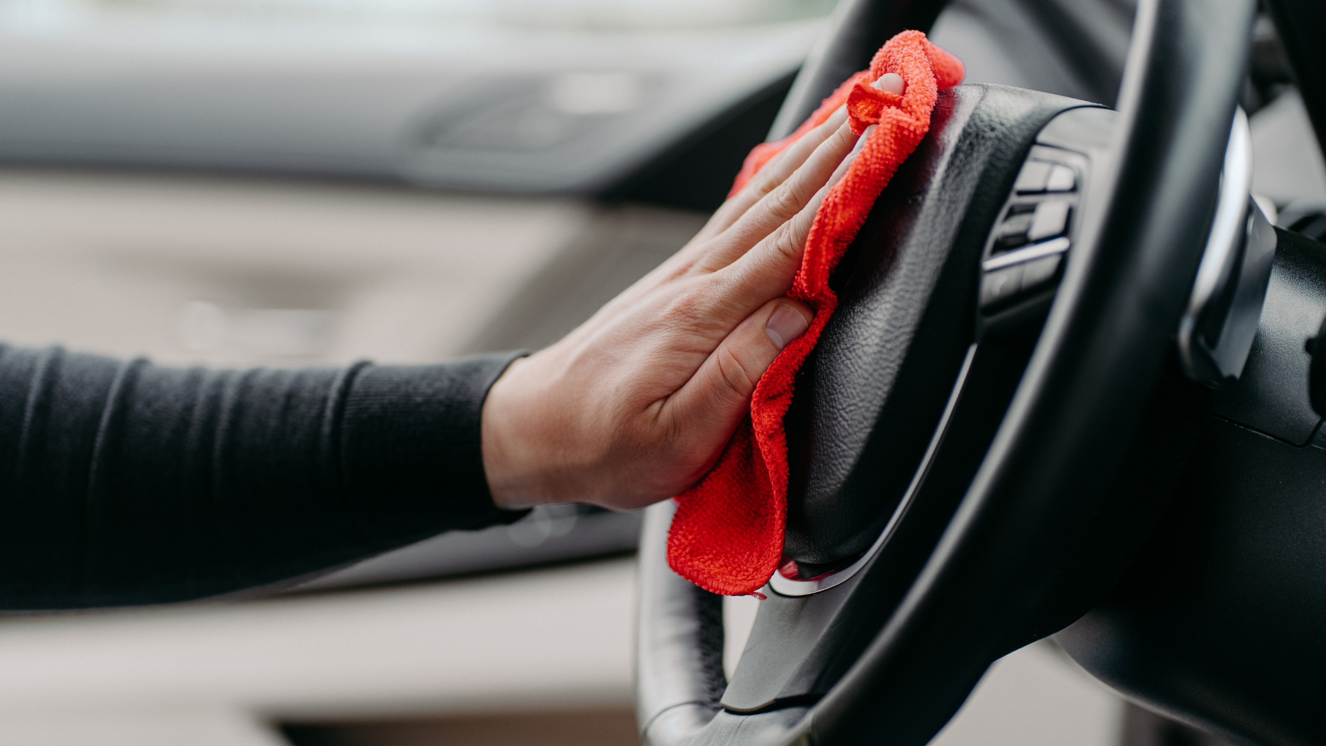a person cleaning a car steering wheel with a red cloth