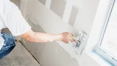 A person smoothing sections of drywall with a squaring tool