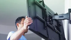 A man adjusting the tilt of a TV on a wall mount