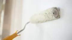 A paint roller with white paint painting a wall