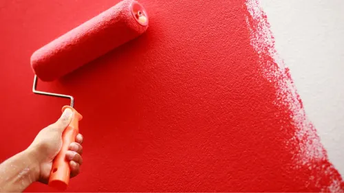 A paint roller with a deep red color painting a wall