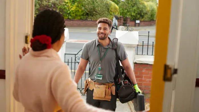 A handyman with tool belts and bags greeting someone at their front door