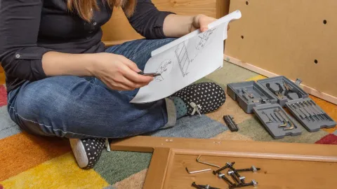 A woman sitting cross legged reading directions to assemble furniture