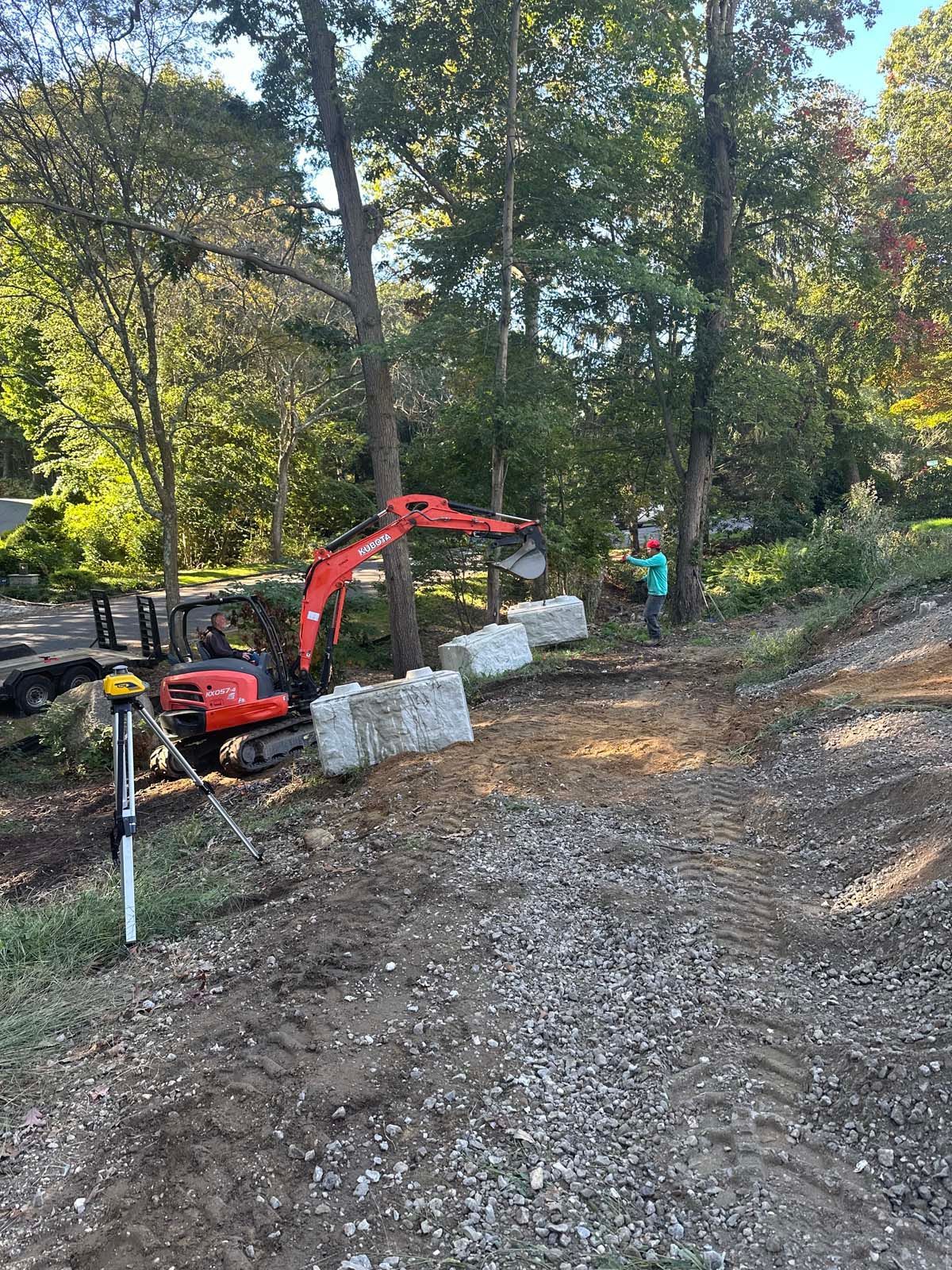 An excavator moves concrete blocks in a wooded area.