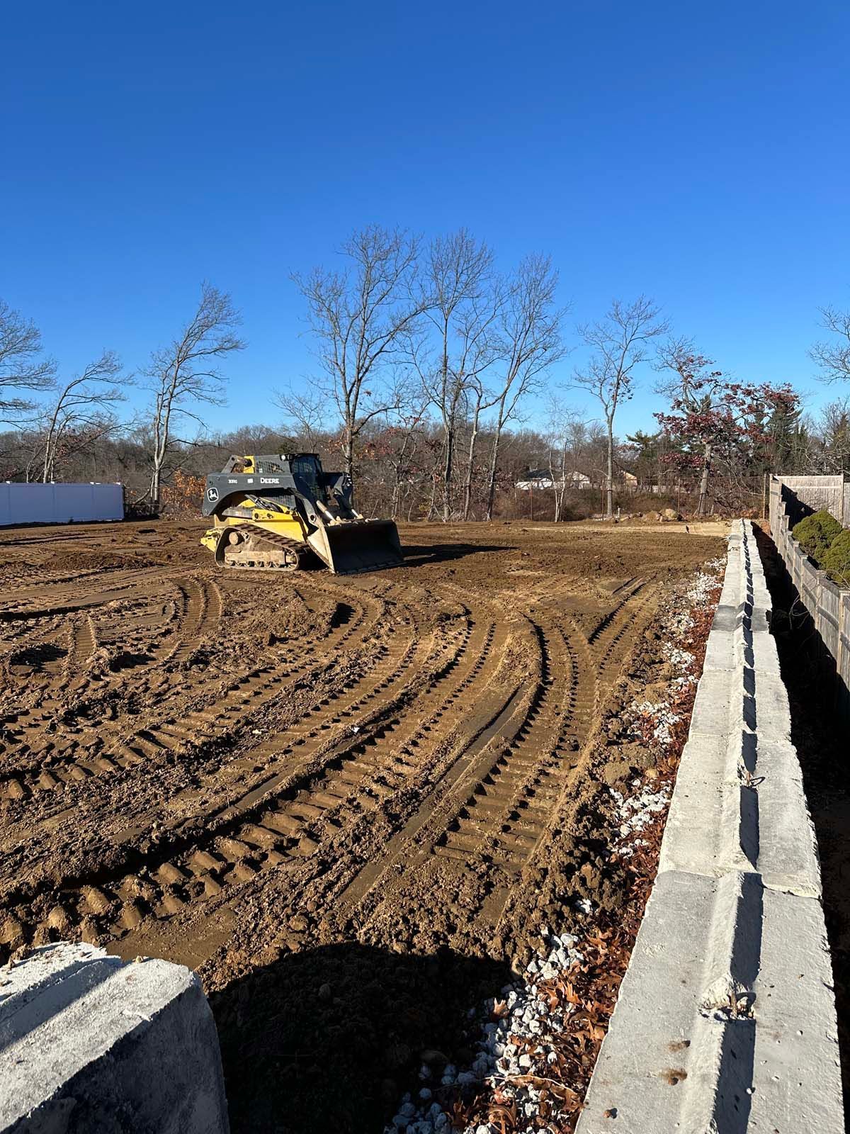 A construction site with a yellow bulldozer on dirt, tracks visible, and a clear blue sky.
