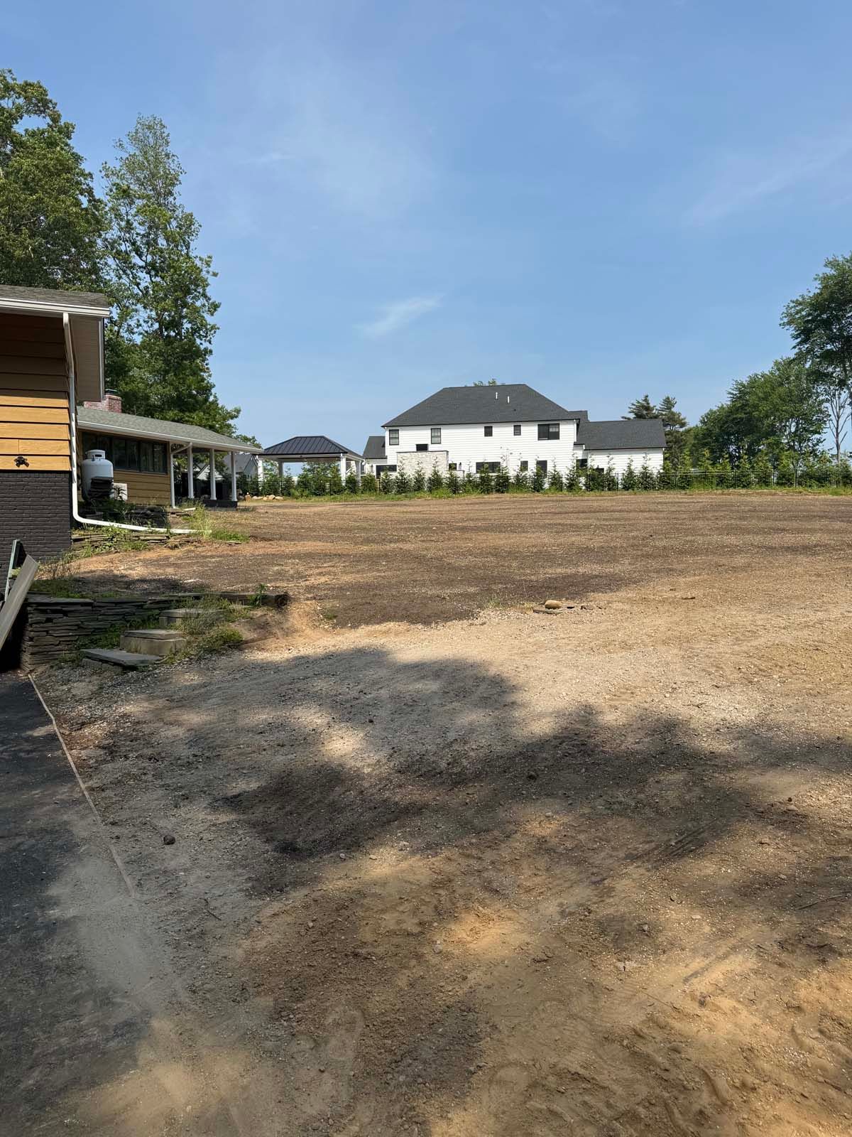 A cleared lot, with a partially built house in the distance under a blue sky.