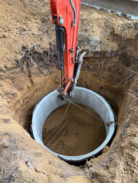 An excavator placing a concrete ring into a circular hole.
