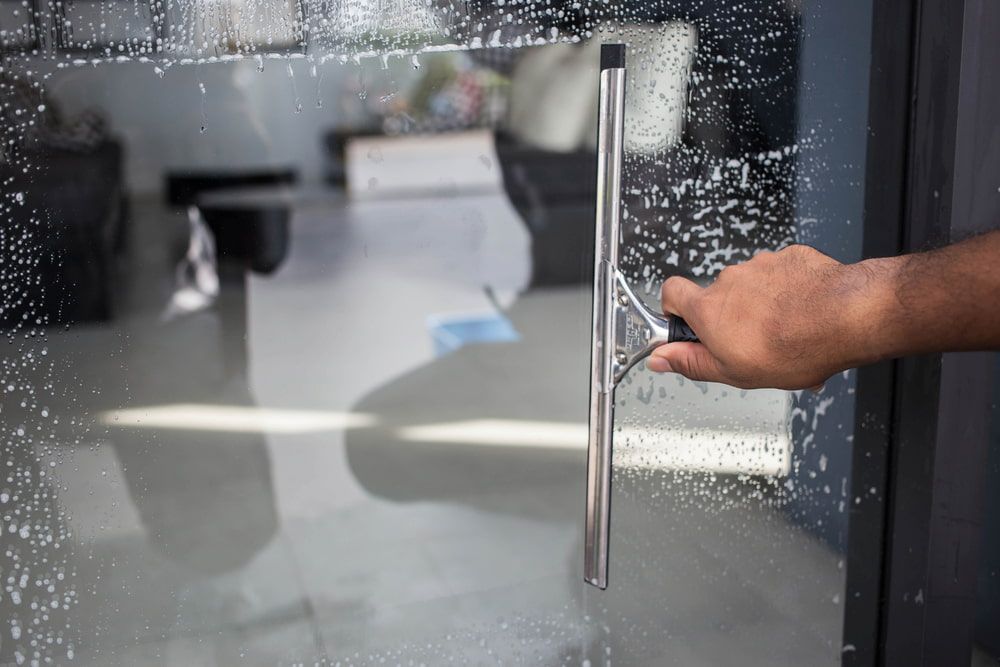 A Person is Cleaning a Glass Door With a Squeegee — Alice Springs Carpet Cleaning In Alice Springs, NT
