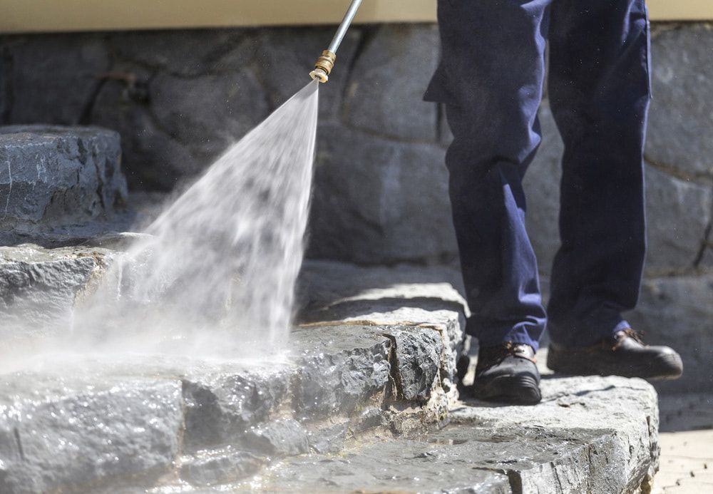 A Person is Using a High Pressure Washer to Clean a Stone Wall — Alice Springs Carpet Cleaning In Alice Springs, NT
