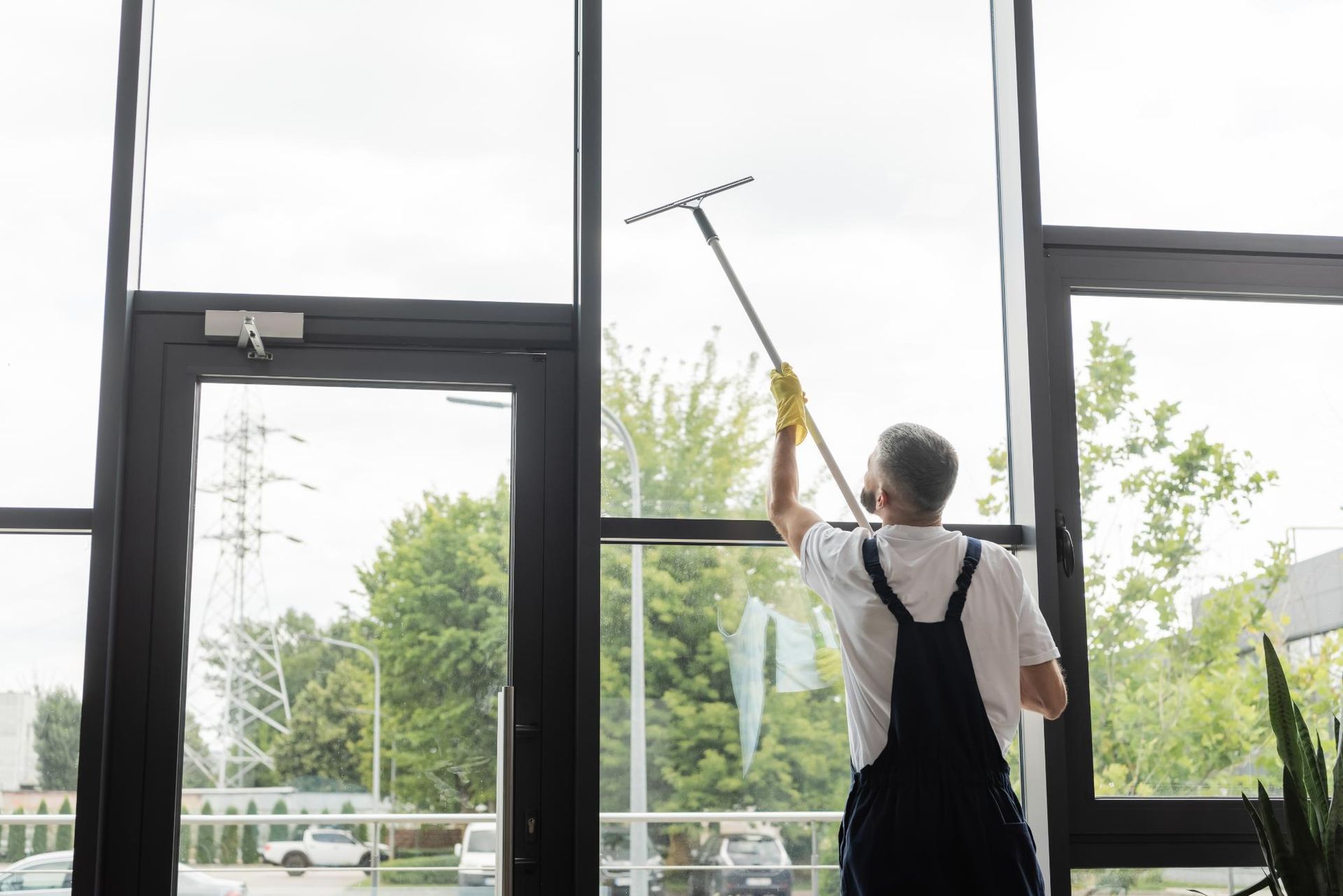 A Man is Cleaning a Window With a Squeegee — Alice Springs Carpet Cleaning In Alice Springs, NT