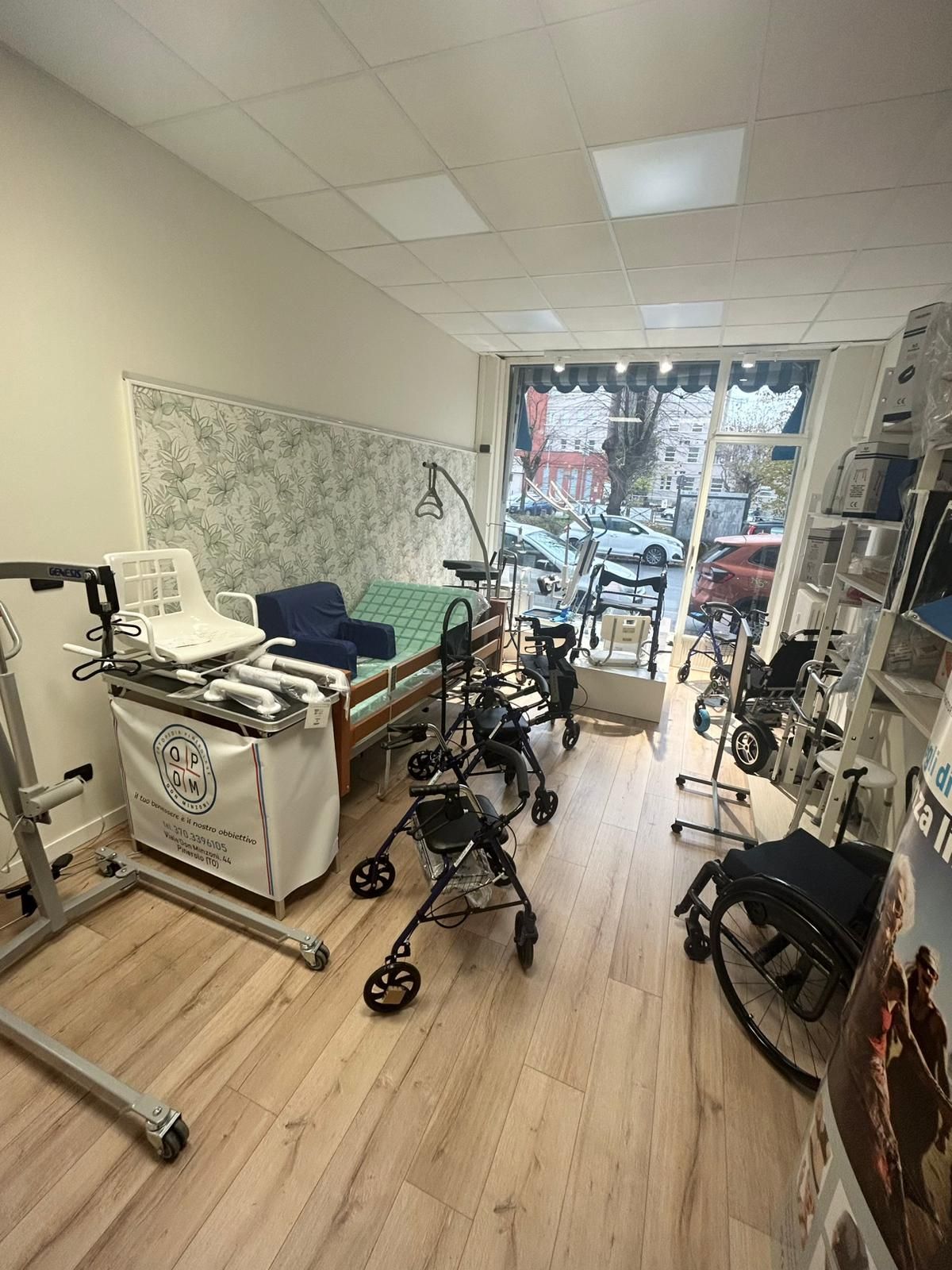 Deambulatore argentato con ruote, altezza regolabile, su un pavimento in legno vicino a carta da parati a motivi.