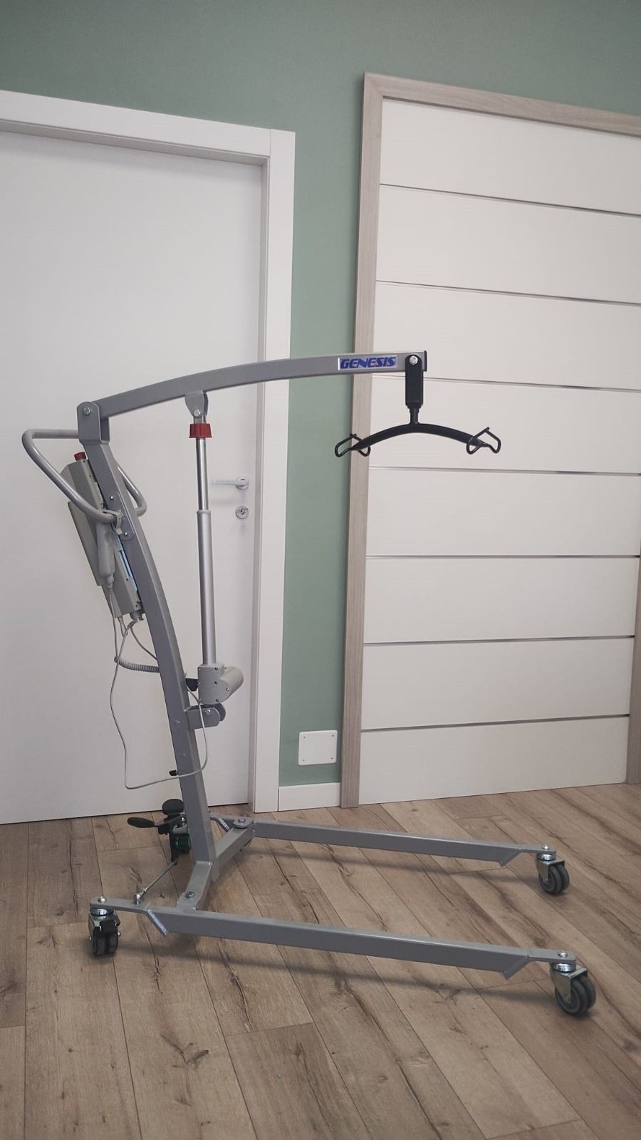 Ascensore grigio per pazienti in una stanza, con una porta bianca e una tenda.