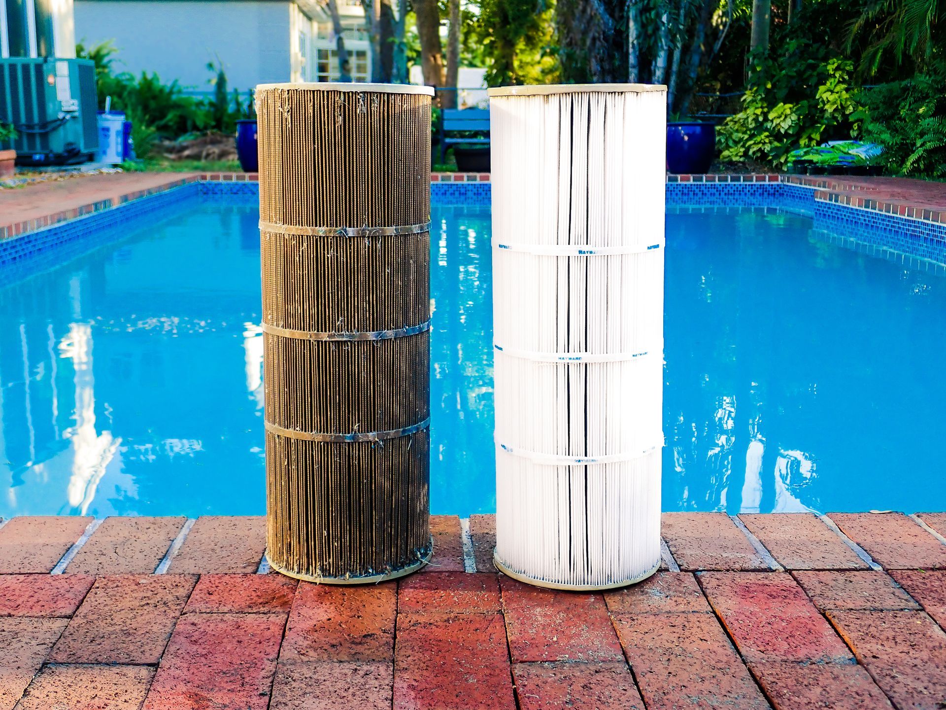 Dirty and clean pool filter cartridges next to a swimming pool.