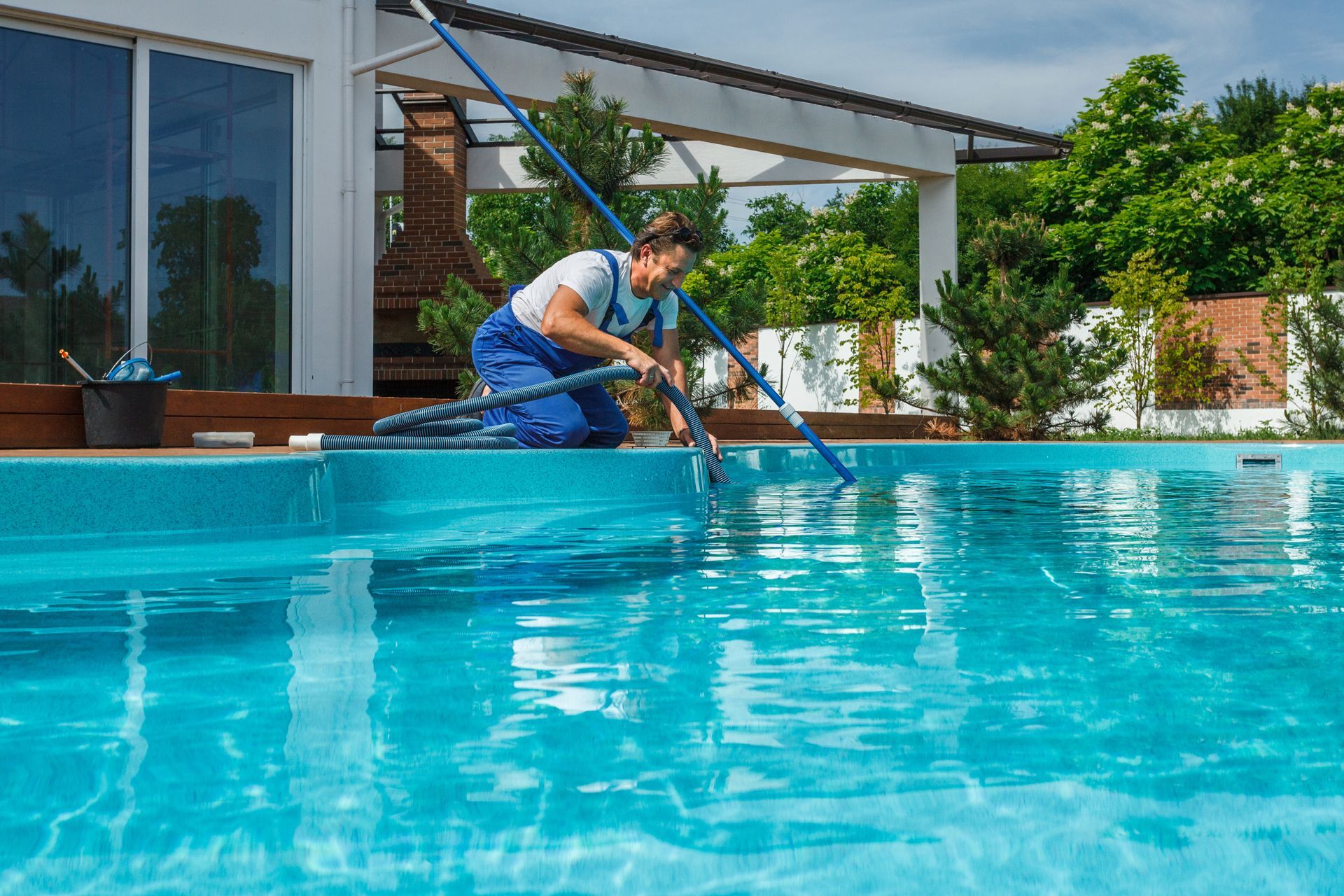 Pool technician cleaning a blue tiled pool with a net and vacuum hose.