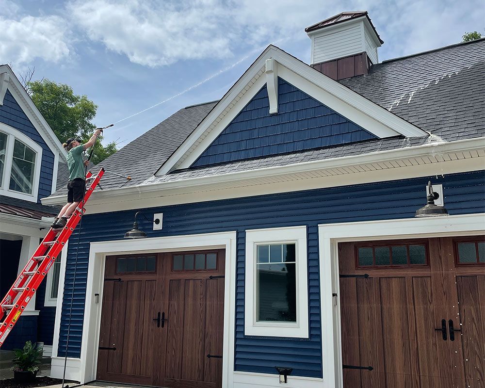a man on a ladder is cleaning the roof of a blue house .