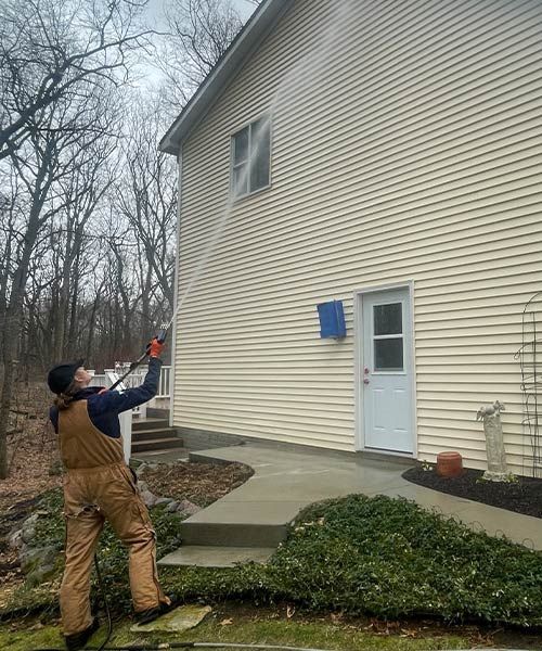 a man is cleaning the side of a house with a pressure washer .