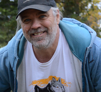 Matt Paproski smiling in wolf enclosure.
