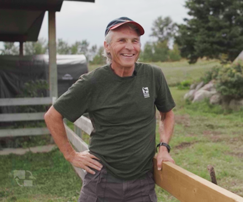 Mammalian ecologist Stan Boutin standing next to a caribou enclosure smiling.
