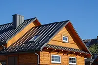 Wooden house with a dark gray metal roof under a clear blue sky.