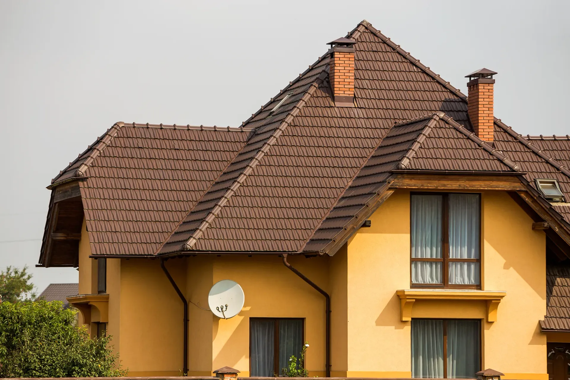 Brown-roofed yellow house with two-story windows, satellite dish, and brick chimney.
