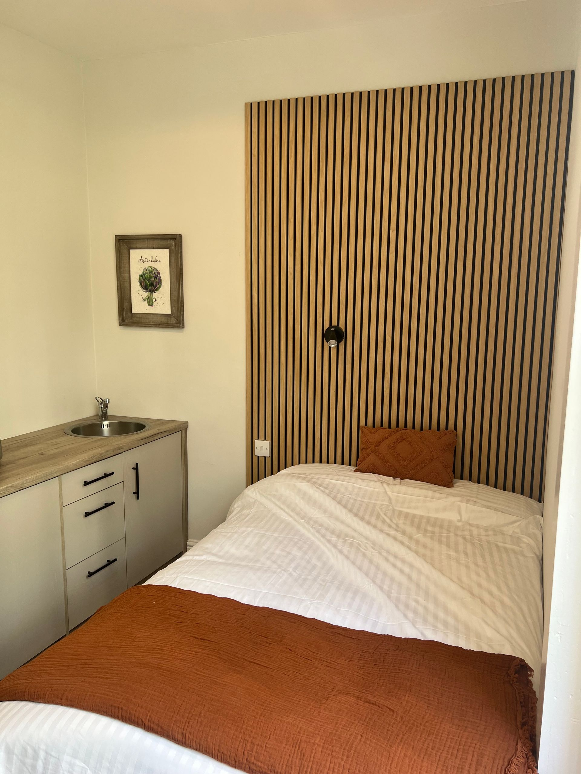 Small bedroom with a single bed, wooden accent wall, and a small sink.