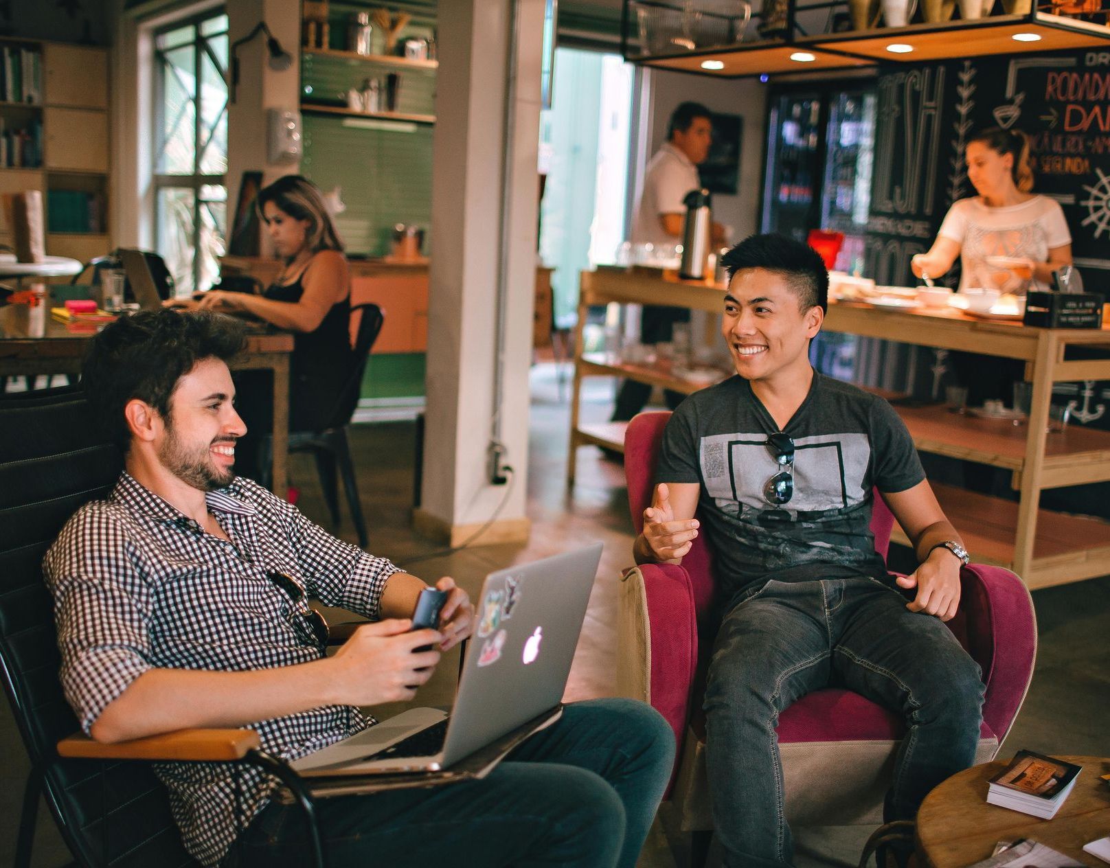 Two men are sitting in chairs with laptops in a room.
