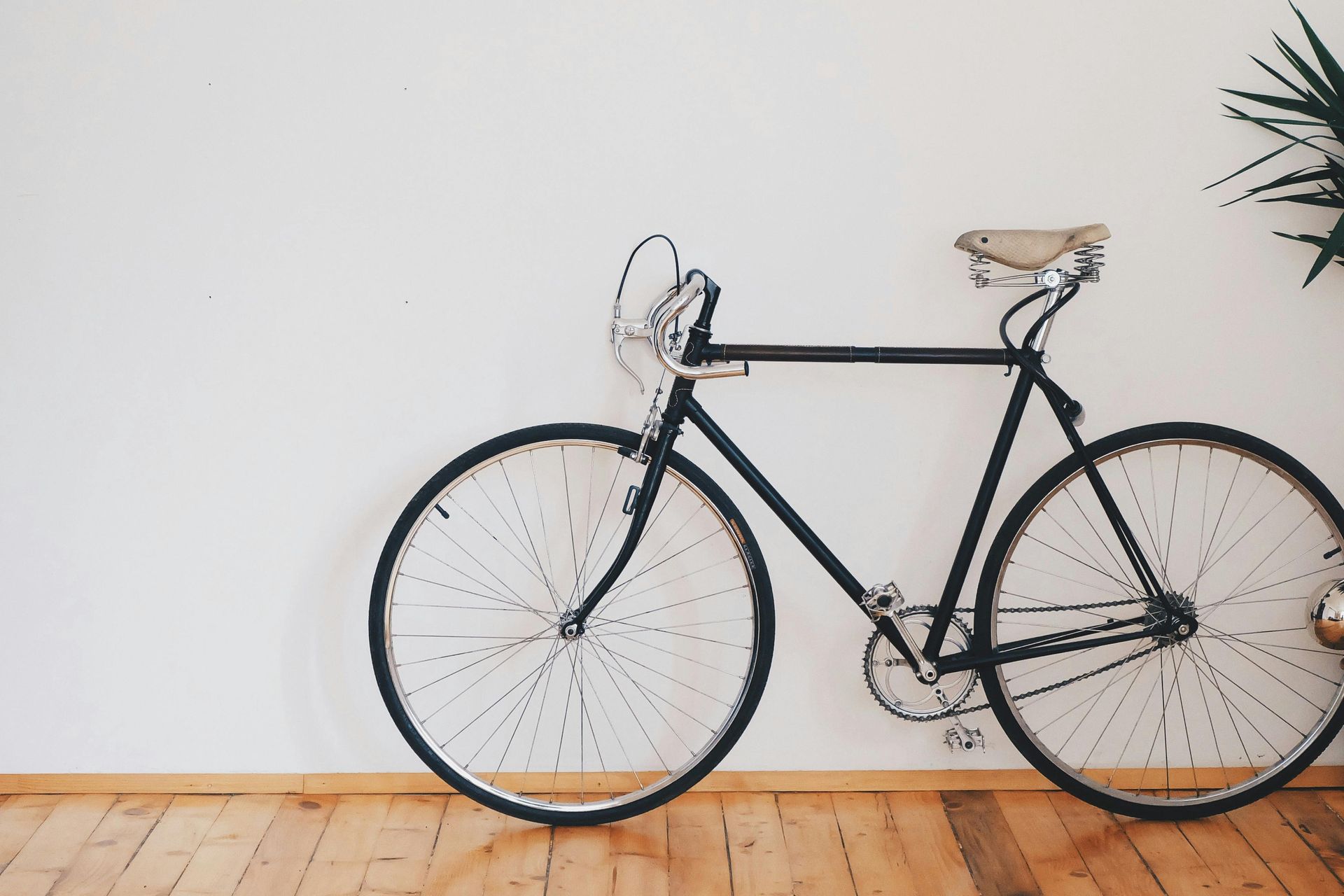 A black bicycle is leaning against a white wall.