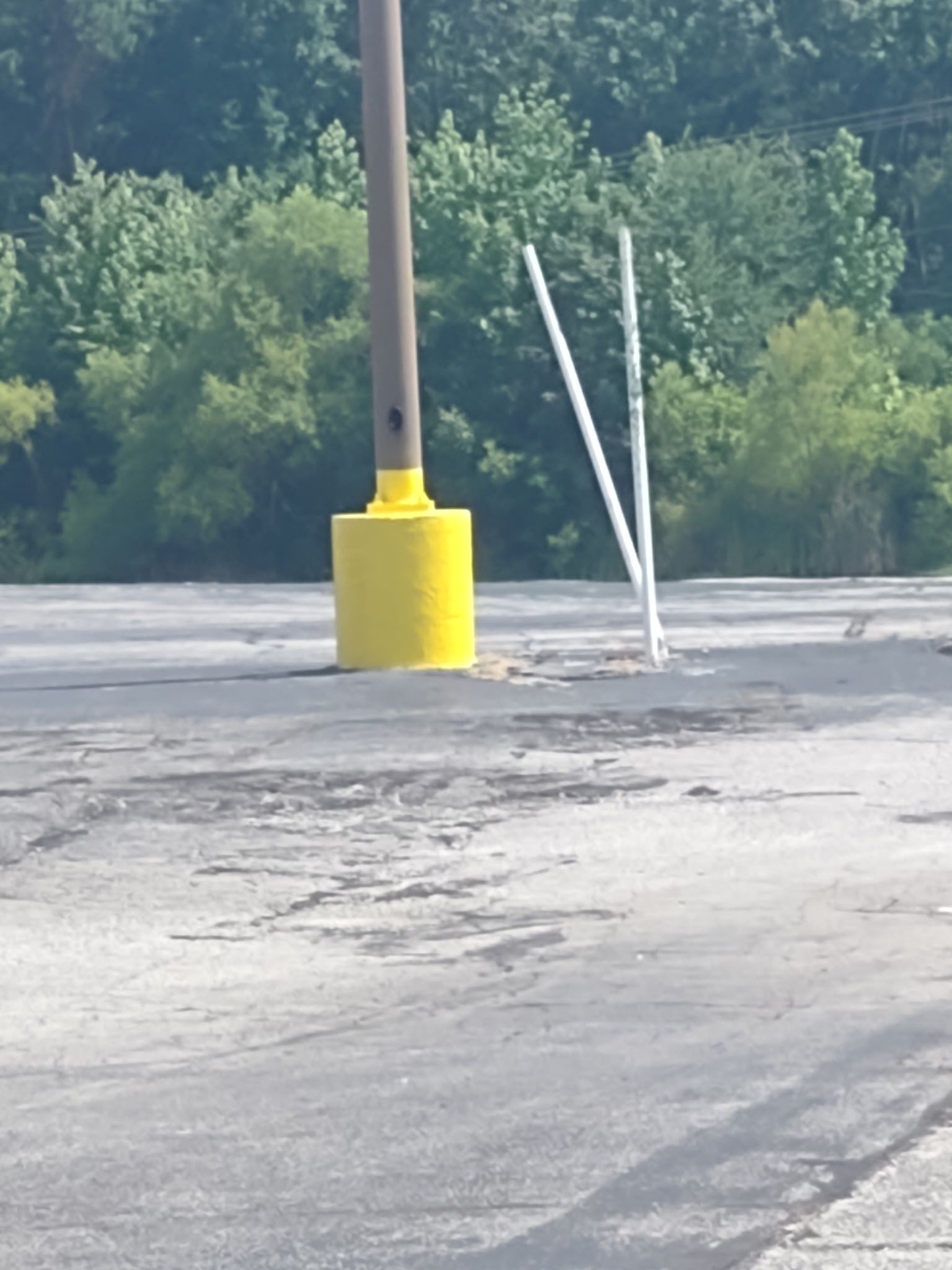 A yellow pole in a parking lot with trees in the background