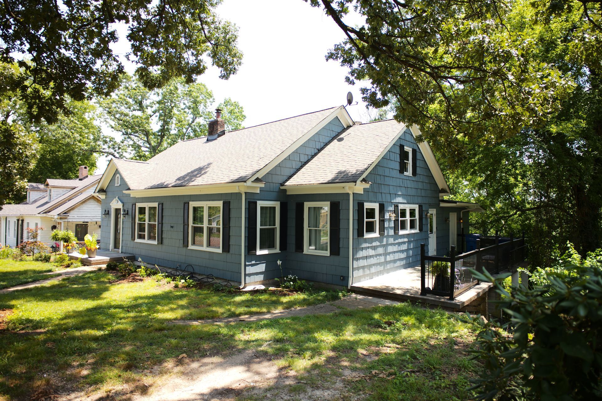 A blue house with white shutters is surrounded by trees